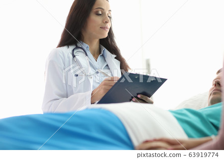 Female doctor stands over man lying hospital bed 63919774