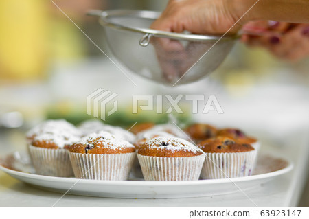 Confectioner sprinkles freshly baked muffins with 63923147