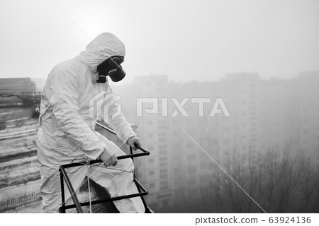 Worker scientist wearing protective coverall and gas mask doing ecological tests on the roof 63924136