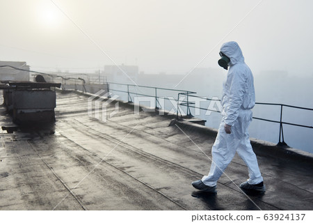 Worker scientist wearing protective coverall and gas mask doing ecological tests on the roof 63924137