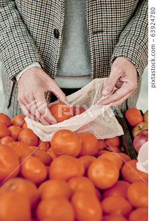 man using a reusable mesh bag at a greengrocer 63924780