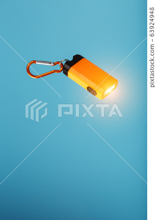 An orange led flashlight with a carabiner glows on An orange led flashlight with a carabiner glows on 63924948