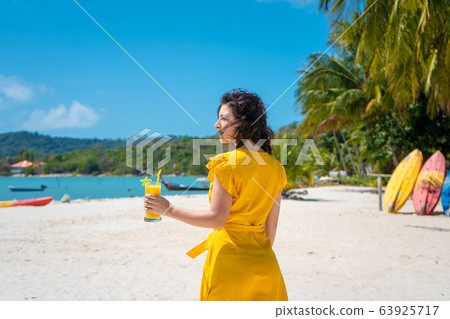 Beautiful girl in a yellow dress drinks fresh 63925717