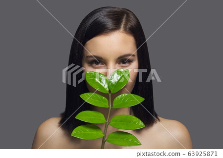 Close-up face of young beautiful woman with green leaf. Beauty portrait of brunette with perfect health skin and hair, natural make-up, gray studio background 63925871