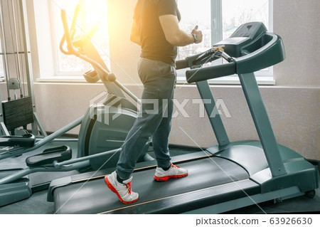 Athletic muscular man running on treadmills in modern sport gym. Fitness, sport, training, people concept. Athletic muscular man running on treadmills in modern sport gym. Fitness, sport, training, people concept. 63926630