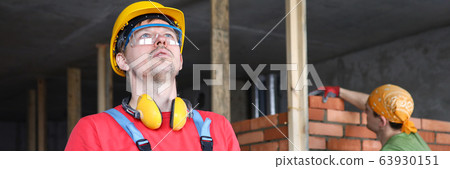 Builder in overalls and helmet makes notes folder 63930151