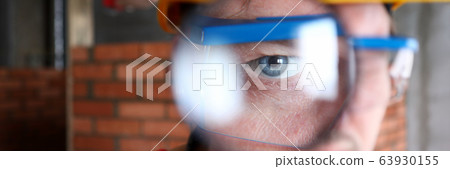 Builder in helmet looks through magnifying glass 63930155