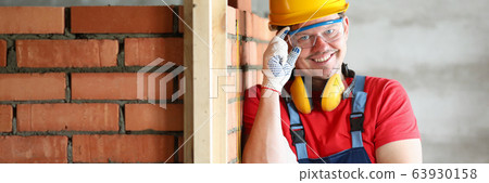 Happy builder stands at brickwork and smiles 63930158