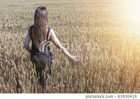 A Woman with a black dress is walking on a wheat 63930419