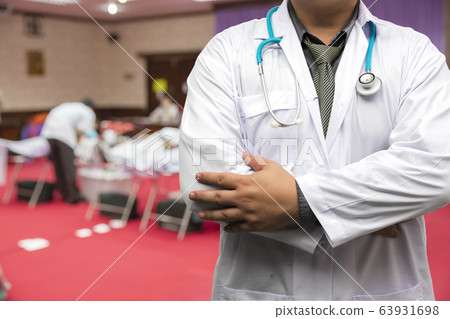 Doctor in gown uniform with stethoscope standing over the chest in blood donor room. Doctor in gown uniform with stethoscope standing over the chest in blood donor room. 63931698