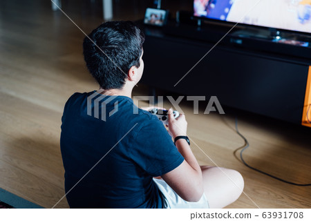 Teenager sitting on the floor at home playing a video game on the console 63931708