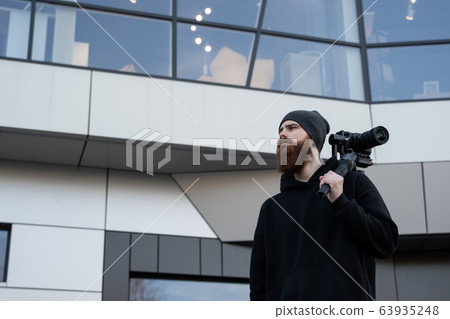 Bearded Professional videographer in black hoodie holding professional camera on 3-axis gimbal stabilizer. Filmmaker making a great video with a professional cinema camera. Cinematographer. Bearded Professional videographer in black hoodie holding professional camera on 3-axis gimbal stabilizer. Filmmaker making a great video with a professional cinema camera. Cinematographer. 63935248