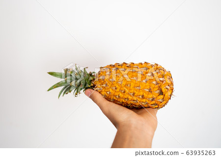 Female hand holding ripe pineapple on a white background. 63935263