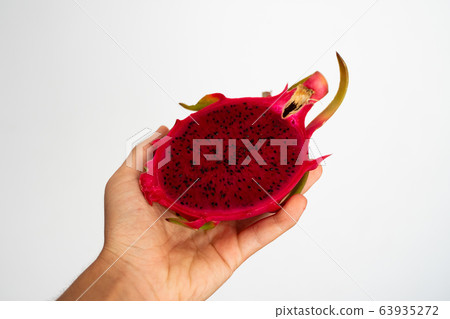 Female hands holding a half of the ripe red dragon fruit on white background. 63935272