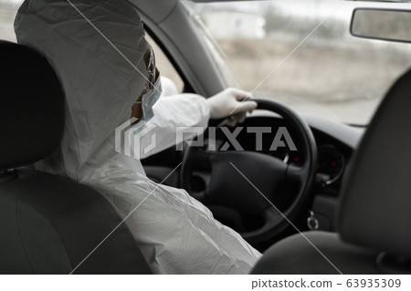 Man in protective suit, medical mask and rubber gloves for protect from bacteria and virus is driving a car. Protective mask while quarantine, world pandemic, covid 19, coronavirus, infection. Man in protective suit, medical mask and rubber gloves for protect from bacteria and virus is driving a car. Protective mask while quarantine, world pandemic, covid 19, coronavirus, infection. 63935309