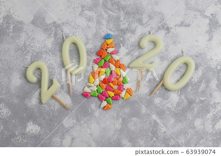 Candles in the shape of numbers 2020 as a symbol of the new year next to christmas shaped sparkle candies on a gray table. Top view, flat lay 63939074