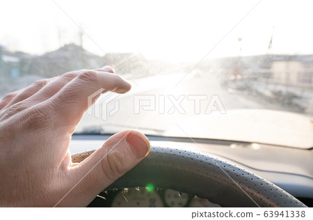 The hand of the driver of the car covers the sunlight, which blinds the person to see the road situation 63941338