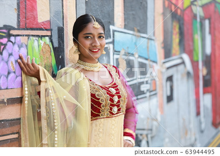 Indian woman wearing a smiling sari in front of a mural on the street [India] [Sari] 63944495