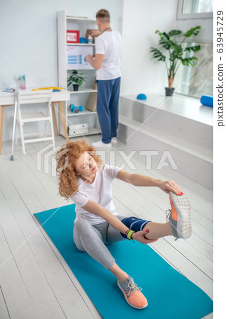 Female patient sitting on mat and stretching Female patient sitting on mat and stretching 63945729