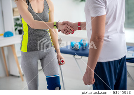 Male physiotherapist shaking hands with female patient holding crutch 63945958