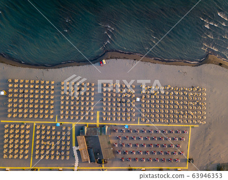 Aerial view of sandy beach with yellow sunbeds and wooden umbrellas at sunset Aerial view of sandy beach with yellow sunbeds and wooden umbrellas at sunset 63946353