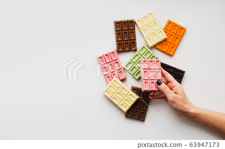 Woman with bright manicure holds in his hand chocolate of various colors and colored fillings with slices of fruit nuts Woman with bright manicure holds in his hand chocolate of various colors and colored fillings with slices of fruit nuts 63947173