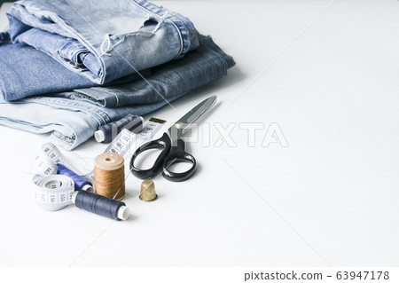 Handicraft, clothing repair. Ripped blue jeans sewing accessories white background. The concept of economical things. 63947178