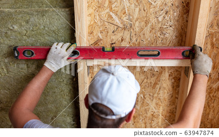 A worker measures a wooden workpiece with a meter. A worker measures a wooden workpiece with a meter. 63947874