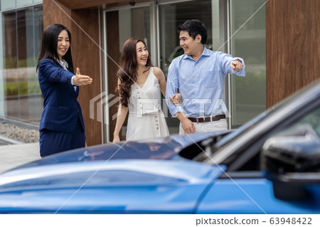 Asian Saleswoman welcoming the couple customer to checking the car infront of showroom, Asian Saleswoman welcoming the couple customer to checking the car infront of showroom, 63948422