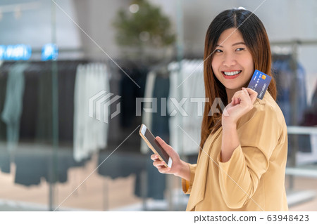 Portrait Asian woman using credit card with smart mobile phone for online shopping in department store over the clothes shop store background, technology money wallet and online payment concept Portrait Asian woman using credit card with smart mobile phone for online shopping in department store over the clothes shop store background, technology money wallet and online payment concept 63948423