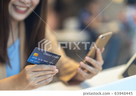 Closeup Asian woman using credit card with mobile for online shopping in department store over the clothes shop store background, technology money wallet and online payment concept, credit card mockup Closeup Asian woman using credit card with mobile for online shopping in department store over the clothes shop store background, technology money wallet and online payment concept, credit card mockup 63948445