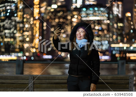Asian woman in Winter suit using smart mobile phone for selfie over the photo blurred bokeh of New york Cityscape beside the east river background, USA downtown, career concept 63948508