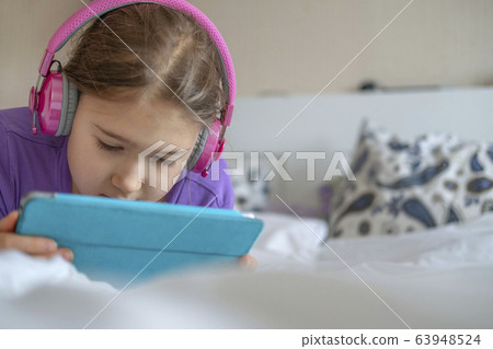 Girl in pink headphones with tablet device Girl in pink headphones with tablet device 63948524
