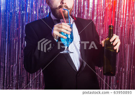 Club party and holidays concept - Close-up of elegant handsome man in a expensive suit holds blue cocktail on shiny background. Club party and holidays concept - Close-up of elegant handsome man in a expensive suit holds blue cocktail on shiny background. 63950893