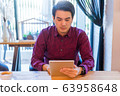 Young asian freelancer working from home and using tablet while sitting the wooden table. 63958648