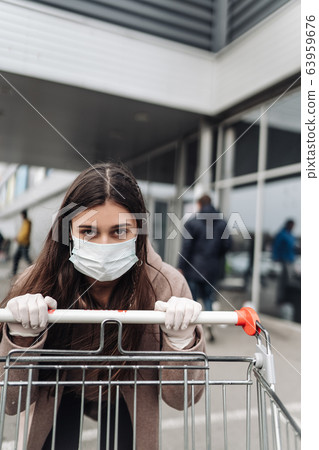 Young woman wearing protection face mask against coronavirus 2019-nCoV pushing a shopping cart. Young woman wearing protection face mask against coronavirus 2019-nCoV pushing a shopping cart. 63959676
