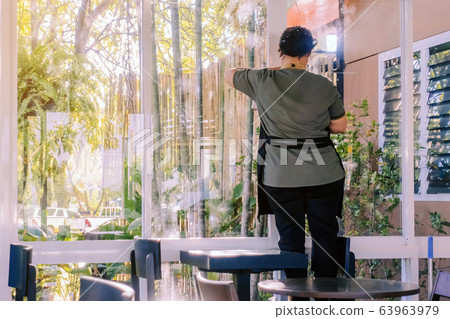 Back view of maid closes the glass window to turn on the air conditioner in the coffee shop. 63963979