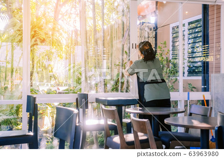 Back view of maid closes the glass window to turn on the air conditioner in the coffee shop. Back view of maid closes the glass window to turn on the air conditioner in the coffee shop. 63963980