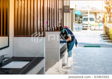 Female janitor using fabric and a detergent cleaning sink and tap in front of the male toilet. Female janitor using fabric and a detergent cleaning sink and tap in front of the male toilet. 63963982