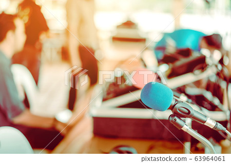 Two microphones with blue and red sponges placed on a stand with earphones on the table with blur image of the audio technician was installing and testing the sound system in the background. 63964061