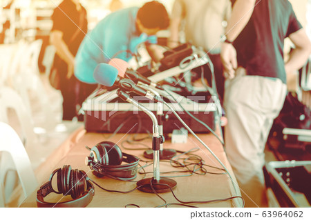 Two microphones with blue and red sponges placed on a stand with earphones on the table with blur image of the audio technician was installing and testing the sound system in the background. 63964062