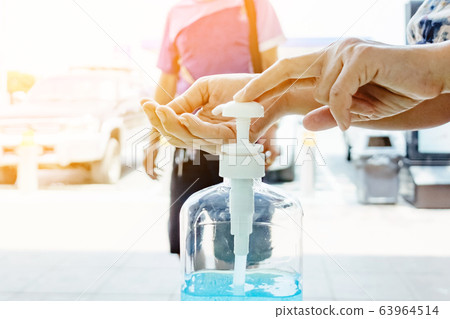 Woman uses her hand to press hand sanitizer bottle to clean her hand at wayside in the city. Concepts of Flu virus, Covid-19 (Coronavirus disease). Selective focus on alcohol gel bottle. 63964514