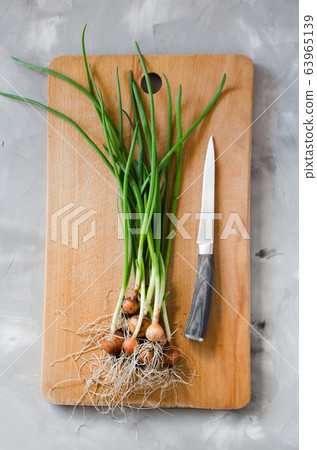 Freshly picked organic spring onions with roots and kitchen knife on a wooden cutting board. Freshly picked organic spring onions with roots and kitchen knife on a wooden cutting board. 63965139