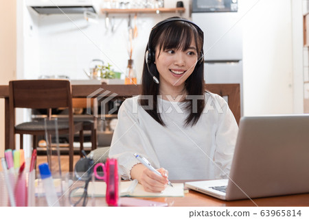 Young woman talking on a personal computer while wearing earphones at home Young woman talking on a personal computer while wearing earphones at home 63965814