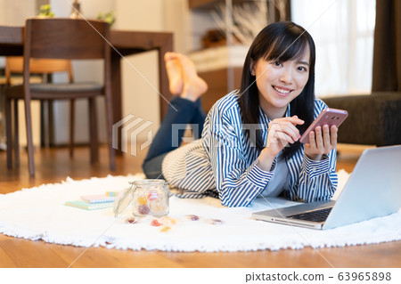 Young woman looking at smartphone while lying in the living room Young woman looking at smartphone while lying in the living room 63965898