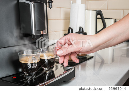 hand takes a glass Cup of hot coffee from the coffee machine 63965944
