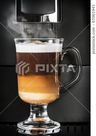 cappuccino from the coffee machine is poured into a glass Cup 63965945
