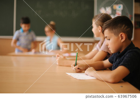 Education, elementary school. Learning and people concept - group of school kids with pens and notebooks writing test in classroom 63967506