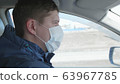 Guy is driving a car. The medical mask on the face. People use extra protection against coronavirus. 63967785