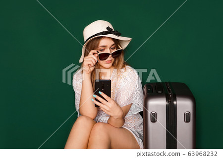 Beautiful girl sits near a suitcase. Waiting for departure. Girl with a phone 63968232